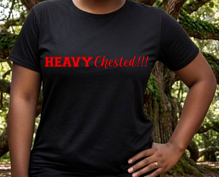 A person wearing a black short-sleeve t-shirt with the text 'HEAVY Chested!!!' printed across the chest in red, standing outdoors in front of a blurred forest background.